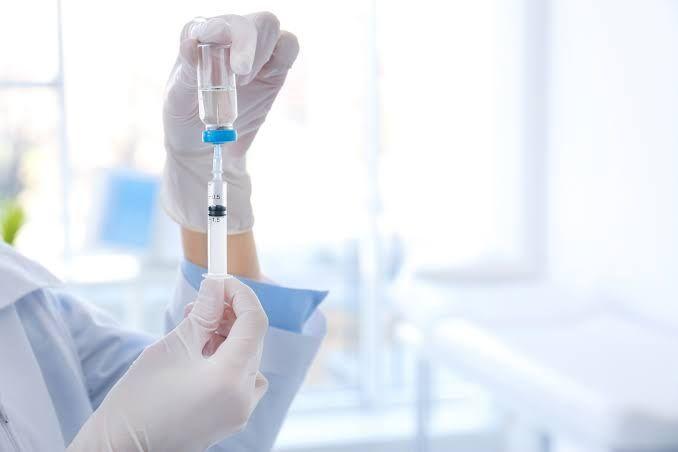 Profissional de saúde preparando seringa com medicamento de um frasco, usando luvas em ambiente clínico