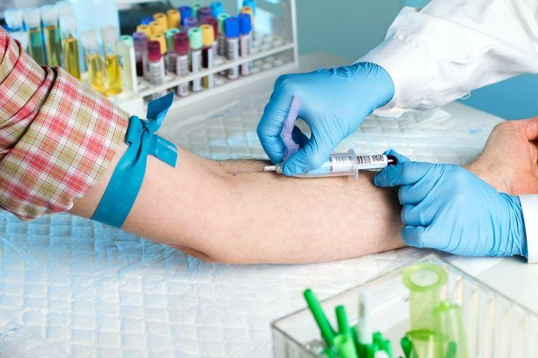 Profissional de saúde realizando coleta de sangue no braço de um paciente, usando luvas e materiais estéreis